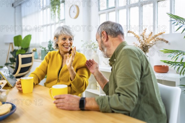 Lovely mature couple enjoying morning coffee at home sitting on living room table and chatting happily