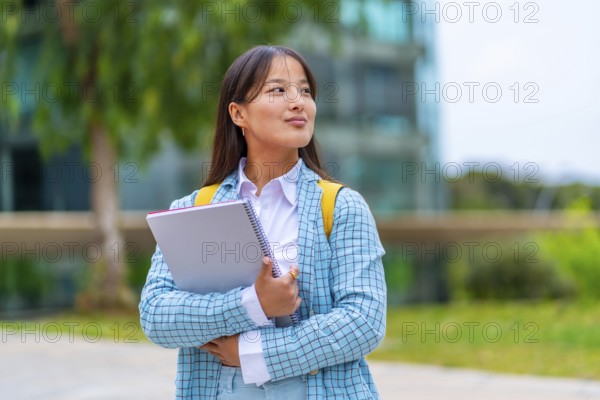 Dreamy chinese student standing outside the university looking away with proud look
