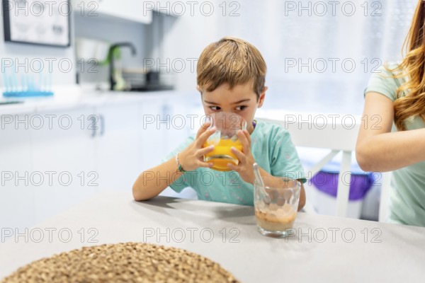 School boy drinking orange juice at home with his mother at the side before going to school