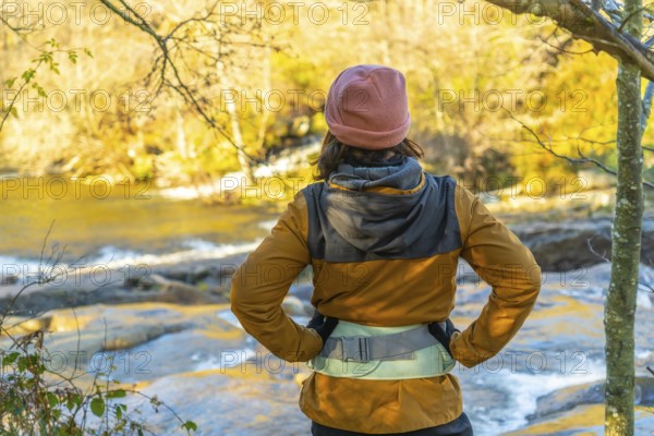 Hiker admiring the serene zaldibartxo pool in gorbeia natural park on a sunny autumn day, surrounded by vibrant foliage and tranquil nature
