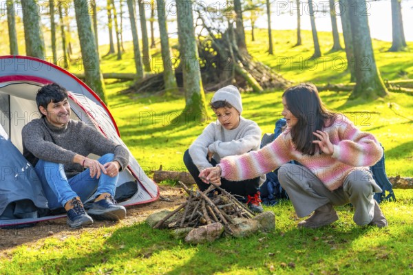 Brother and dad preparing bonfire next to camping tent in an alpine forest