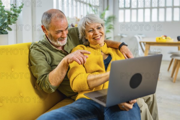 Mature woman lying on her husband sharing laptop on sofa in a cozy modern apartment