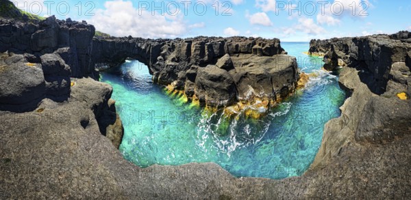 Panoramic view of rugged lava rock formations with a natural arch over turquoise sea under blue sky, A Porta do Diabo, Sao Miguel Island, Azores, Portugal, Europe