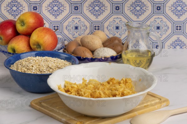 Grated apple in a bowl in front of oat flakes, eggs and honey
