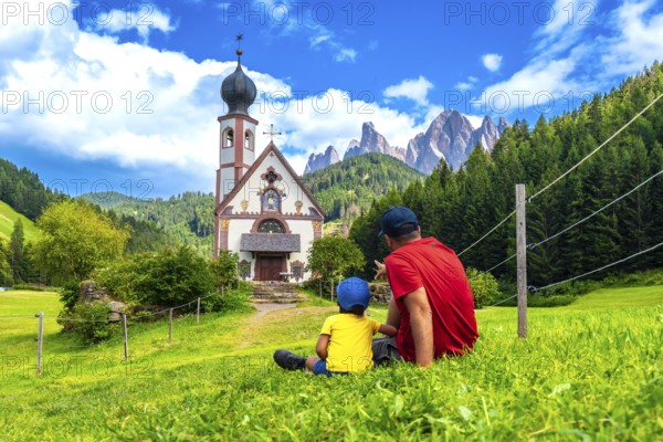 Father and son admiring the stunning view of the idyllic st. Magdalena church in the picturesque val di funes, framed by the dolomites