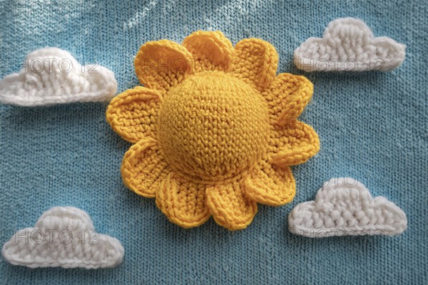 Crocheted yellow sun and white clouds on a light blue knitted background, AI generated, AI generated