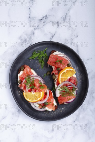 Sandwich with freshly smoked salmon, on black bread, with cottage cheese, with herbs and red onions, capers and pieces of citrus fruits, on a marble countertop, breakfast, no people
