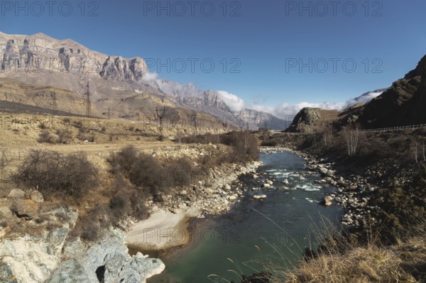 A mountain river in a mountainous rocky area near which there are power lines on the background of epic rocks and a blue sky. Concept of energy supply for mountain residential areas