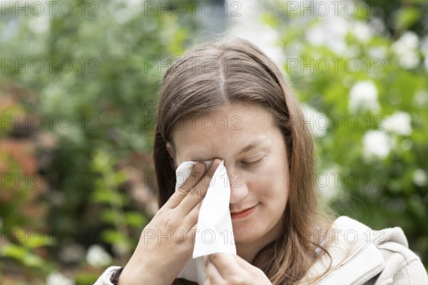Young woman suffers from hay fever and uses a paper handkerchief outdoors, Freiburg, Baden-Württemberg, Germany, Europe