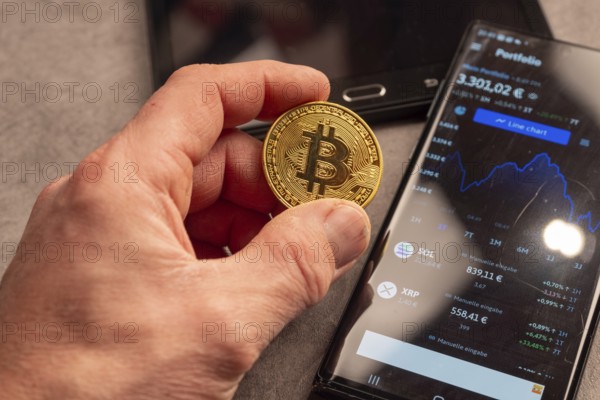 A hand shows a Bitcoin coin next to a smartphone with portfolio data