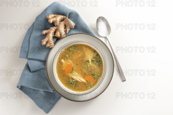 Healthy soup from chicken meat, vegetables and ginger in a bowl on a blue napkin and a gay white background, top view from above, copy space, selected focus