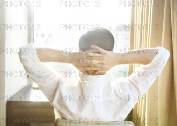 Rear view of young man relaxing on chair at home