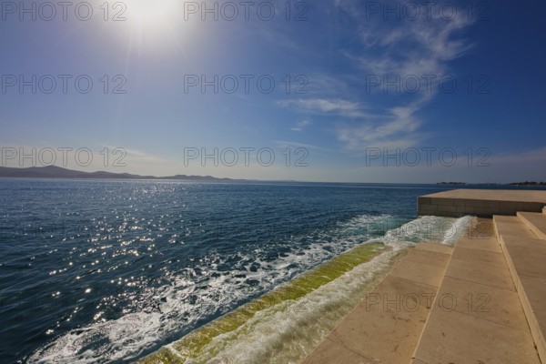 Steps lead to the clear sea under bright sunshine and blue sky, a calm coastal atmosphere, sea organ Zadar Dalmatia Croatia