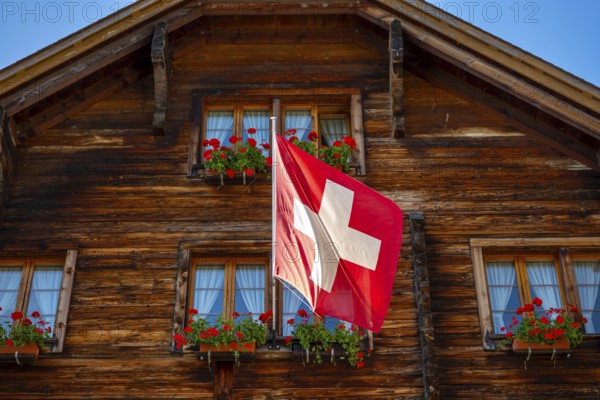 Beautiful Old Town with a Wood House with Flower and Swiss Flag in a Sunny Summer Day in Andermatt, Uri, Switzerland, Europe