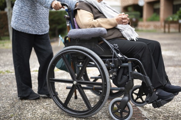 Elderly woman in wheel chair spending time with her daughter in the garden of nursing home. graphy