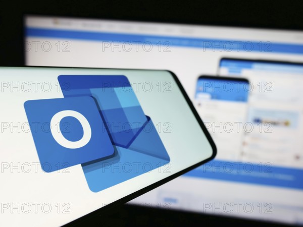 Stuttgart, Germany, 09-21-2023: Mobile phone with logo of email software Microsoft Outlook on screen in front of company website. Focus on center-left of phone display, Europe