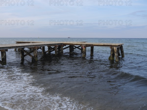An old wooden jetty juts into the sea, surrounded by gentle waves under an evening sky, sopot, baltic sea, poland