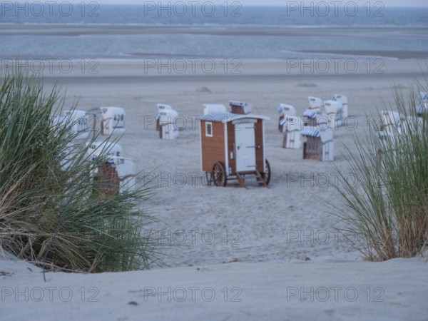 Beach section with scattered beach chairs, sand dunes and grass under a twilight sky by the sea, Spiekeroog, north sea, germany