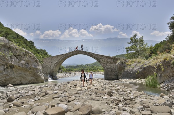 Two young woman walking barefoot in the riverbed over large stones, Ottoman stone bridge, Kadiut Bridge, Lengarica Canyon, Benje, Albania, Europe