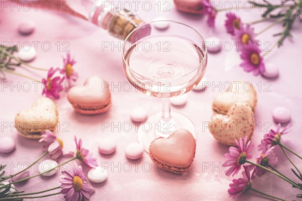 Happy Mothers Day - sweet macarons in heart shape and glass of rose sparkling wine with flowers in pink tone