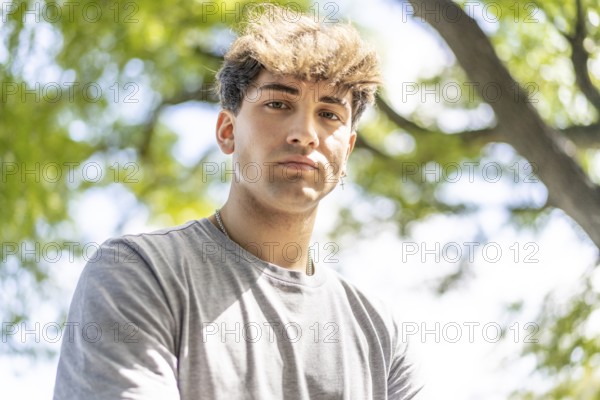 Confident young blonde man portrait, summer trees background.