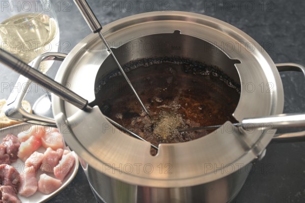 View into a fondue pot with boiling hot oil, long forks, pieces of meat and wine, festive dinner for parties with friends and family, selected focus, narrow depth of field