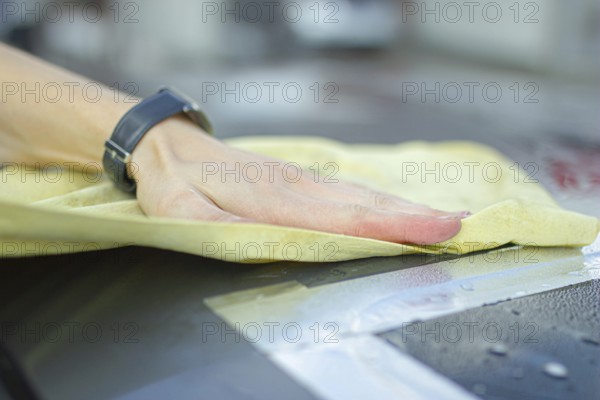 A hand wiping a car surface with a yellow cloth during cleaning