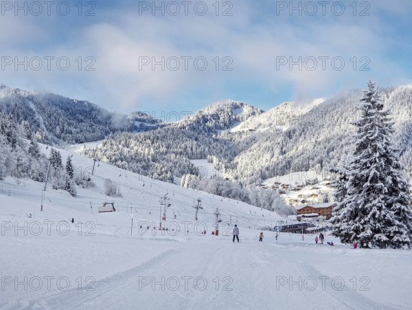 Picturesque snowy mountain landscape with slopes, lifts, and skiers at La Clusaz ski resort, Annecy, France. Snow covered woods and a small village with cabins nestled in the valley
