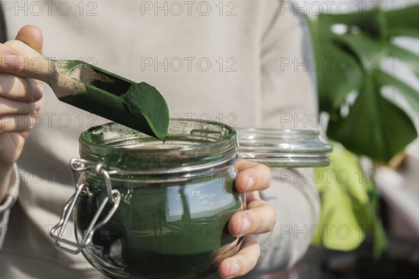 Female hands holding Organic blue-green algae spirulina detox powder in glass jar. Health protein of chlorella. Vitamins and minerals to diet. Prebiotic and antioxidant rich Dietary supplement Seaweed superfood concept
