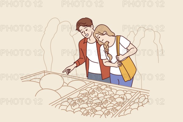 Man and woman do shopping at market and stand near crates of vegetables at farmers fair. Happy couple chooses organic vegetables and fruits to cook delicious food with eco ingredients