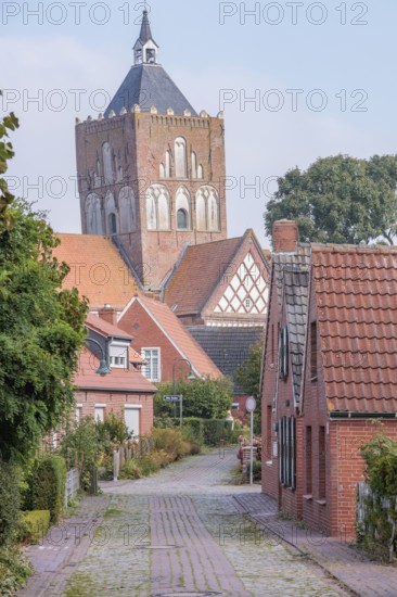Historic village street with brick houses and a large tower in the background, krummhörn, east frisia, germany