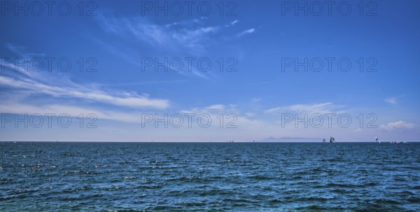 Panoramic beautiful seascape on a bright summer day with few sailing boats afar, great sky with dynamic clouds. Peaceful vacation, meditative, relaxing view. Weekend by sea, beach, contemplation