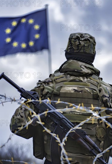 Symbolic image for the threat of war in the EU, a soldier in full combat gear stands in front of an EU flag, behind him a barbed wire fence, AI generated, AI generated