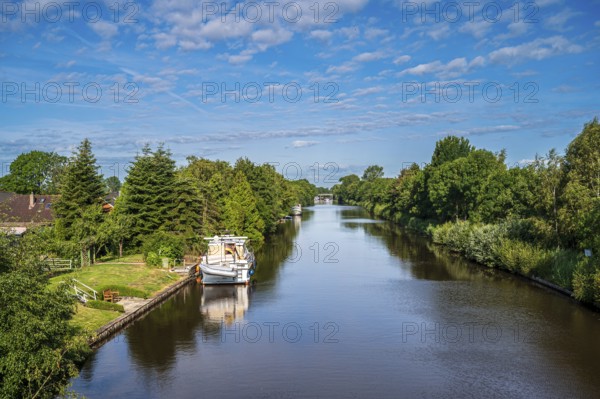 A canal surrounded by lush greenery under a slightly cloudy sky with a boat, Ems-Seitenkanal, Emden, East Frisia, Lower Saxony