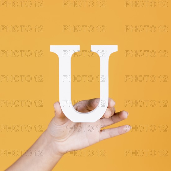 Female hand holding white uppercase alphabet u yellow surface