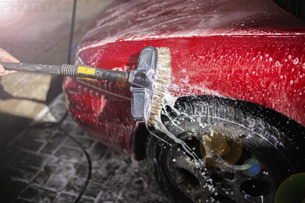 Washing a soapy red car focusing on the side and tire with a brush