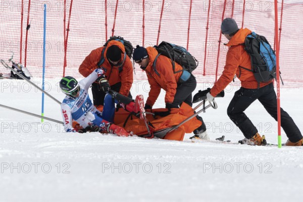KAMCHATKA PENINSULA, RUSSIA, MAR 28, 2019: Rescuers Kamchatka Rescue Squad on alpine ski evacuate injured skier sportsman from mountain on tactical rescue stretchers during competition alpine skiing