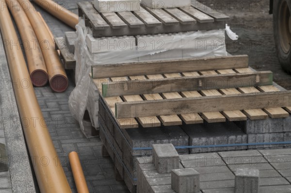 Construction materials including paving stones, orange pipes and wooden pallets laying on a cobblestone street during roadworks