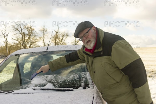 Senior citizen removes frost and snow from car windscreen