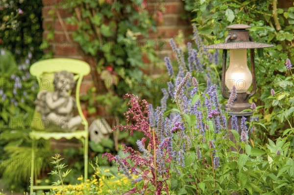 A garden with a statue of an angel on a green chair, surrounded by flowering plants and a burning lamp, Borken, münsterland, germany