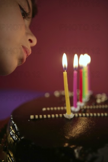 Little girl blowing birthday chocolate cake candles in a row over red background