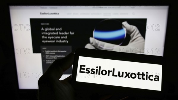 Stuttgart, Germany, 05-21-2022: Person holding smartphone with logo of French eyewear company EssilorLuxottica S.A. on screen in front of website. Focus on phone display, Europe