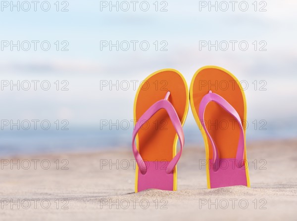 Close up of a pair of colorful orange flip flops in sand at the beach under blue sky background