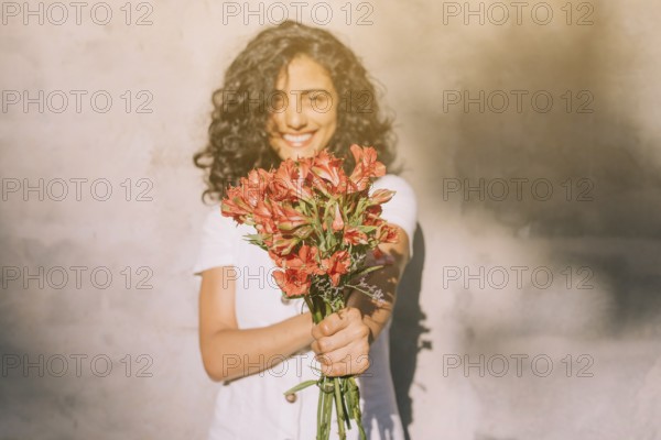 Young woman standing against wall holding (alstroemeria) red flower bouquet hands