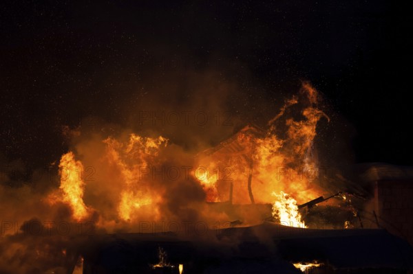 Arson or nature disaster, burning fire flame on wooden house roof