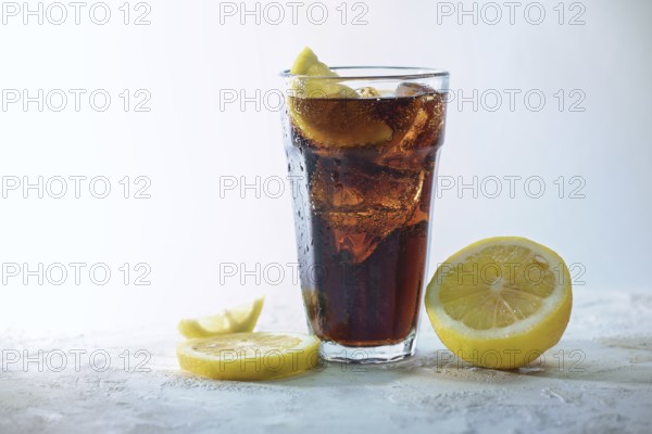 Fresh cola with ice cubes and lemon slices in a drinking glass against a light blue gray background, refreshing sweet caffeine drink, copy space, selected focus, narrow depth of field