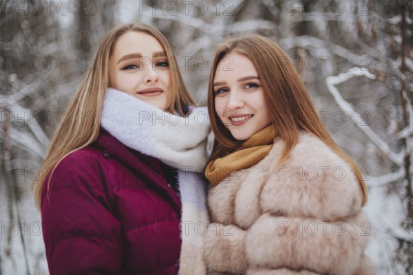 Two happy female friends enjoying snowing weather outdoors, women best friends in winter clothes down jackets laughing and having fun while walking on city street in winter during Christmas holidays