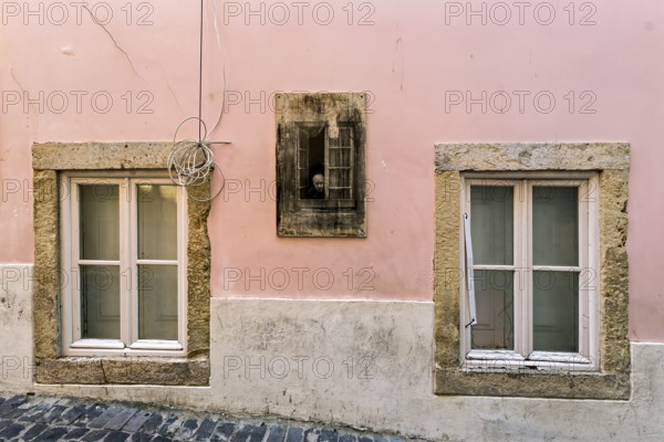Facade of an old building with pastel pink walls and stone-framed windows with closed wooden shutters, Alfama, Lisbon