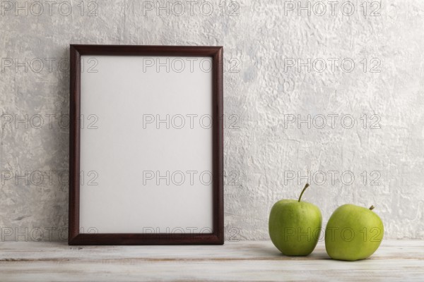 Brown wooden frame mockup with green apple on gray concrete background. Blank, vertical orientation, still life, copy space