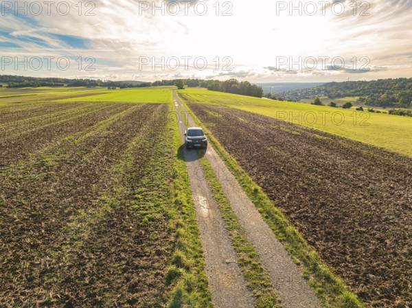 Black car driving on a long, straight country lane through scenic fields under a cloudy sky, car sharing, VW ID5, Calw, Black Forest, Germany, Europe
